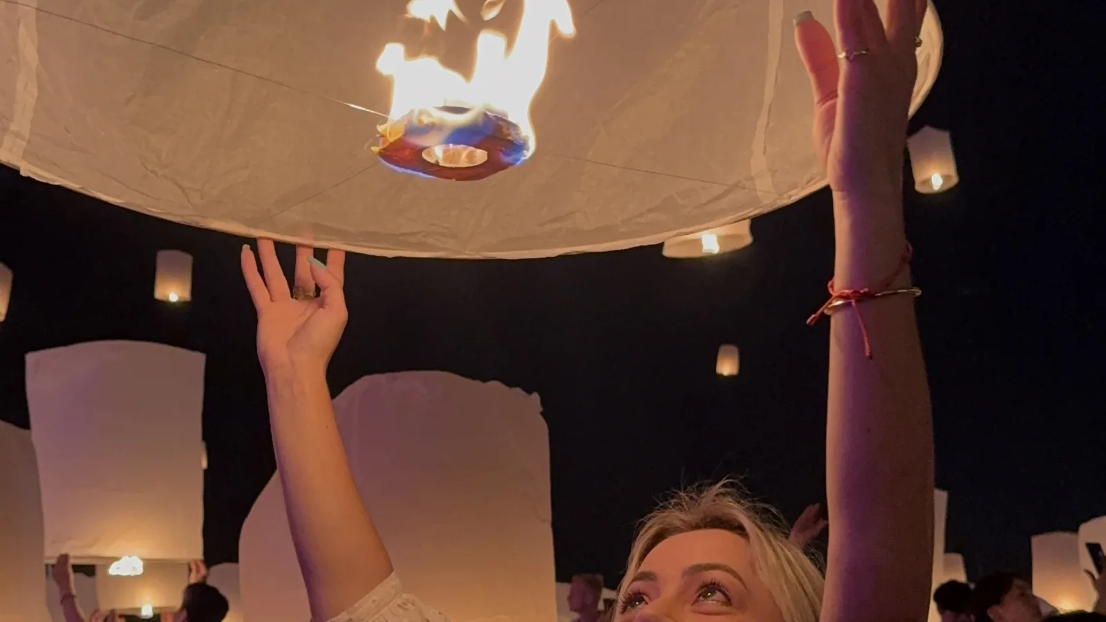 Close-up de uma mulher tailandesa soltando uma lanterna Khom Loi durante o festival das lanternas Tailândia, com a luz da lanterna iluminando seu rosto. MinÁsia 2026.