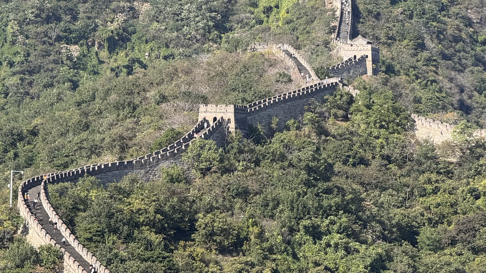 Close-up da muralha da china, destacando os detalhes da estrutura e turistas explorando ao fundo. Atmosfera histórica.