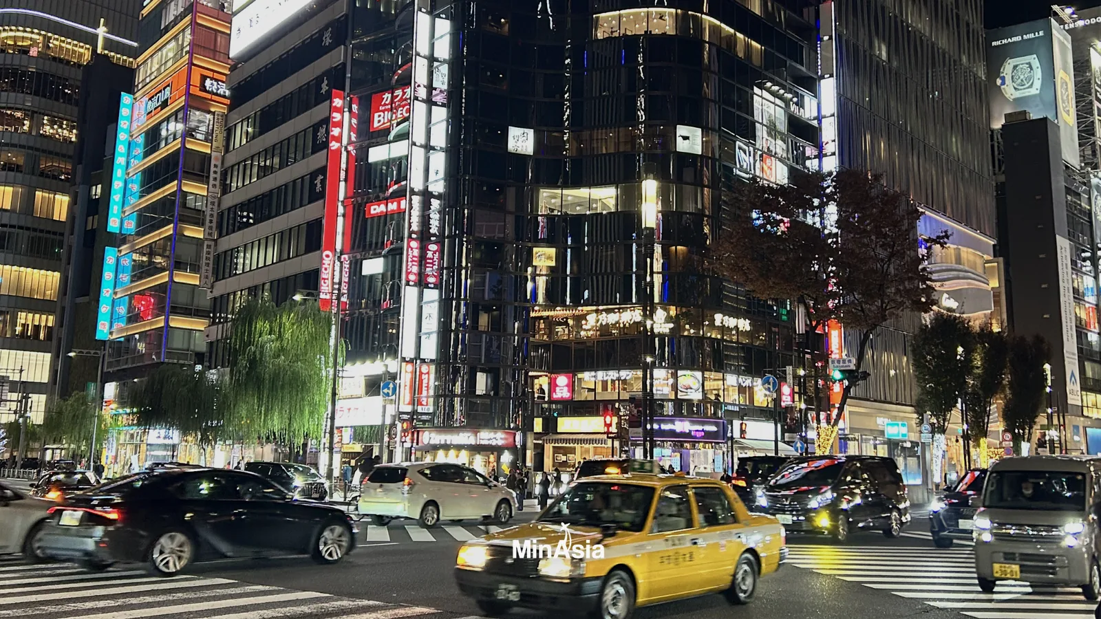 Foto de ângulo alto do shibuya crossing em horário de pico, mostrando a escala e a densidade da multidão. MinAsia Tours em destaque em um banner.