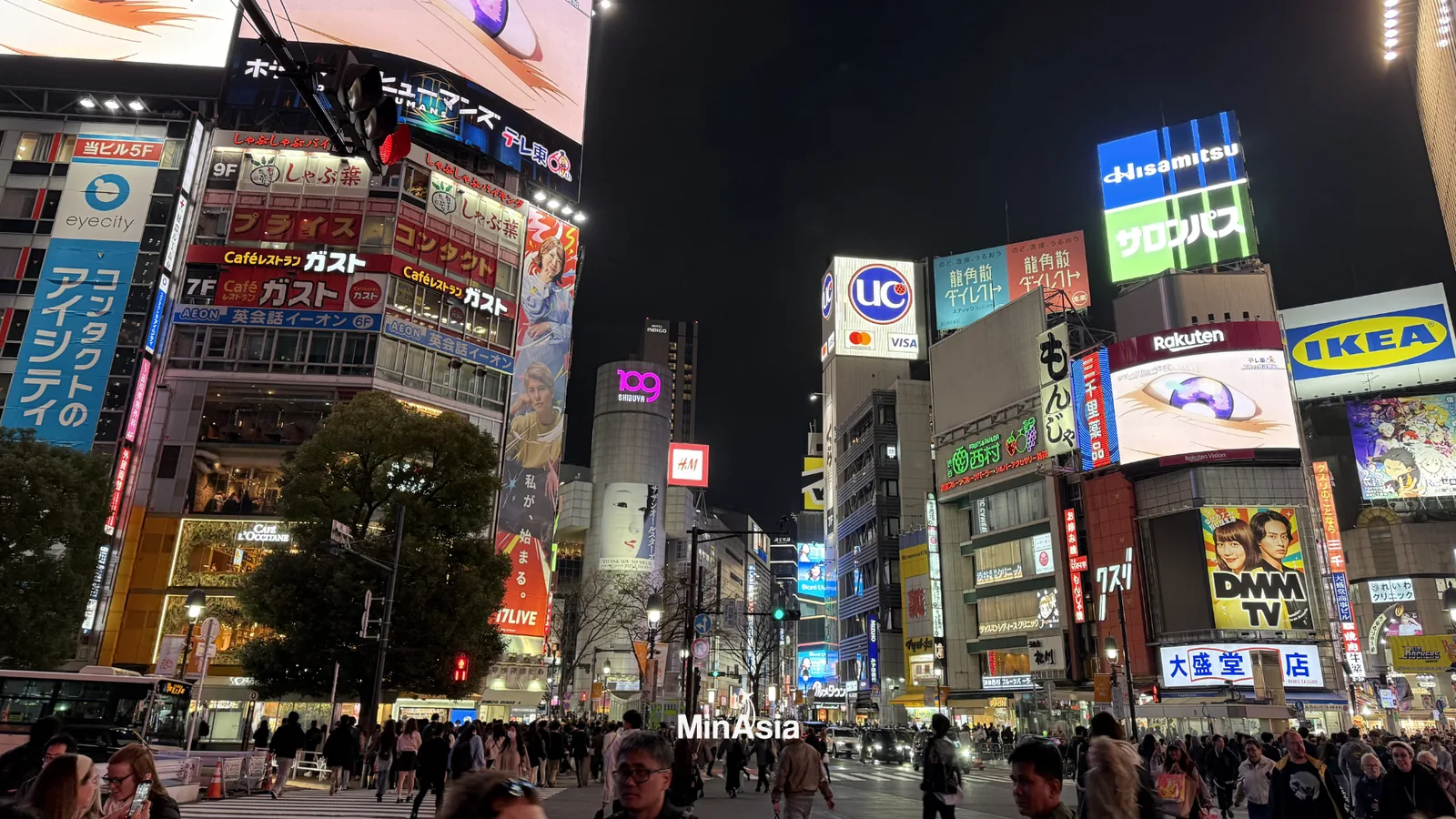 Close-up de pedestres atravessando o shibuya crossing, com foco nas expressões e diversidade. MinAsia e Shibuya aparecem sutilmente em placas e letreiros.